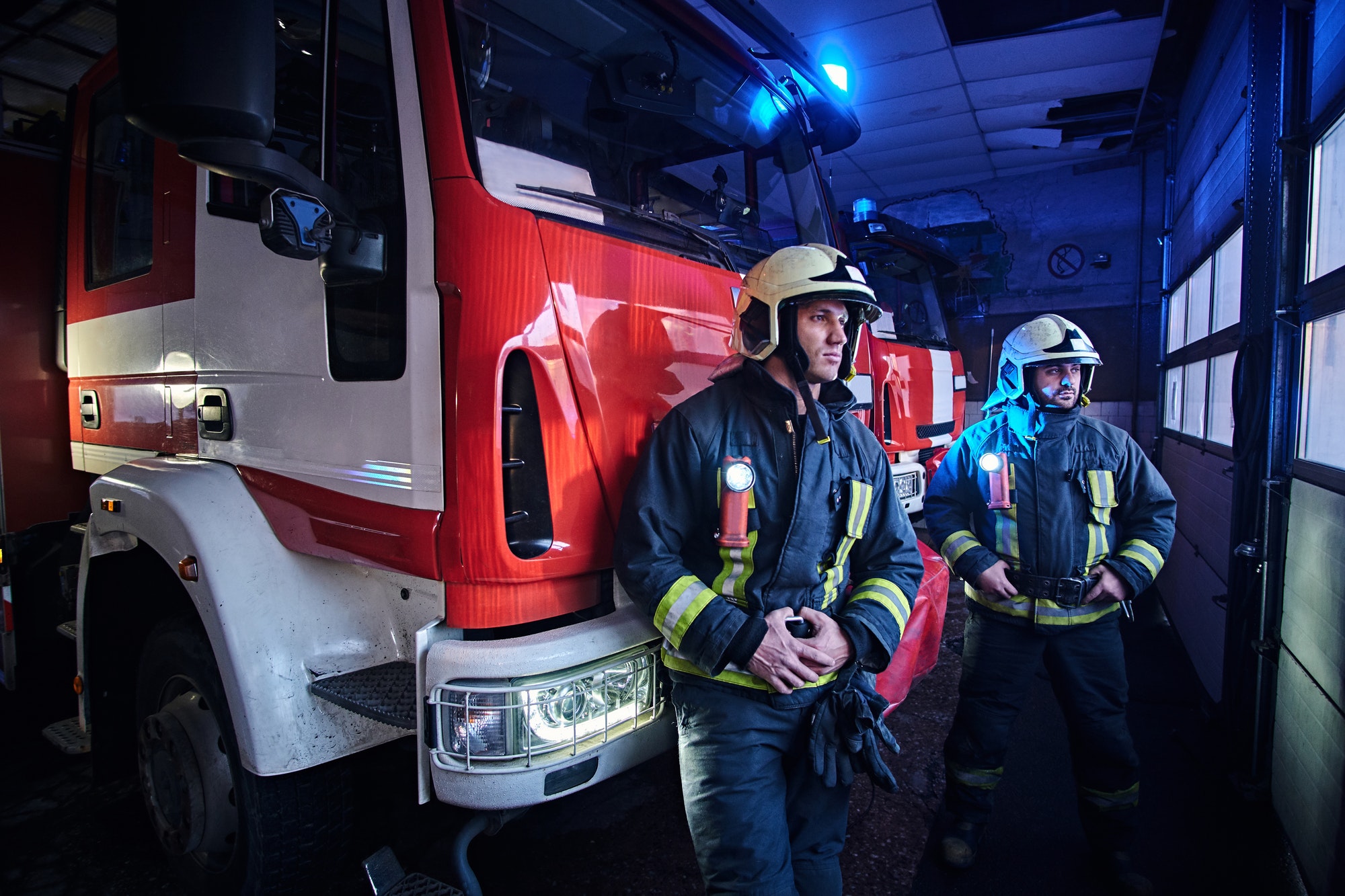 two-firemen-standing-near-the-fire-truck-at-night-in-a-fire-depot-2.jpg