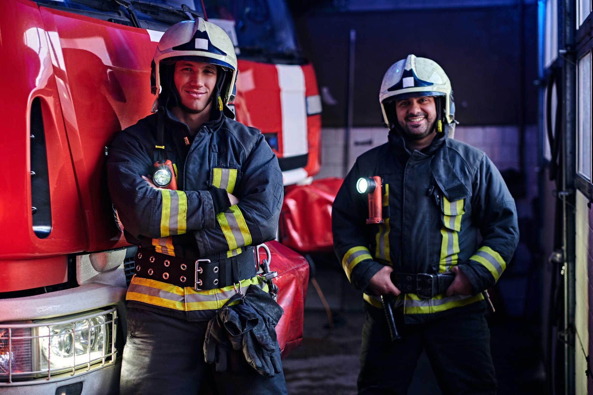 two-firemen-standing-near-the-fire-truck-at-night-in-a-fire-depot.jpg